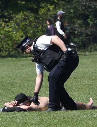 Police officer attending to a person who has collapsed in a park during hot weather.